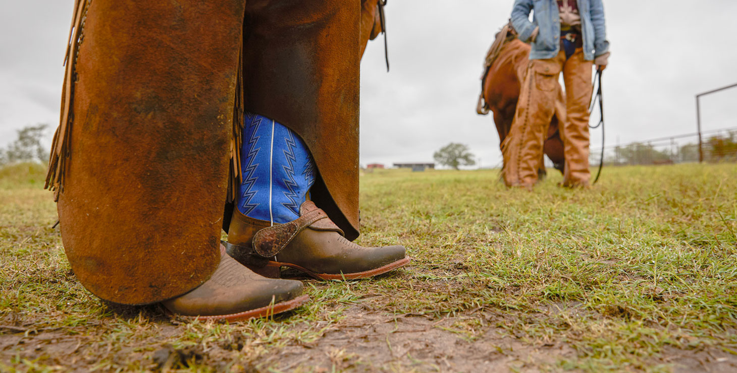 Una foto de un Ranker 13” Western en el frente siendo usado por un vaquero con polainas y posando frente a una vaquera con un sombrero burdeos mirando hacia otro lado en un campo de hierba.